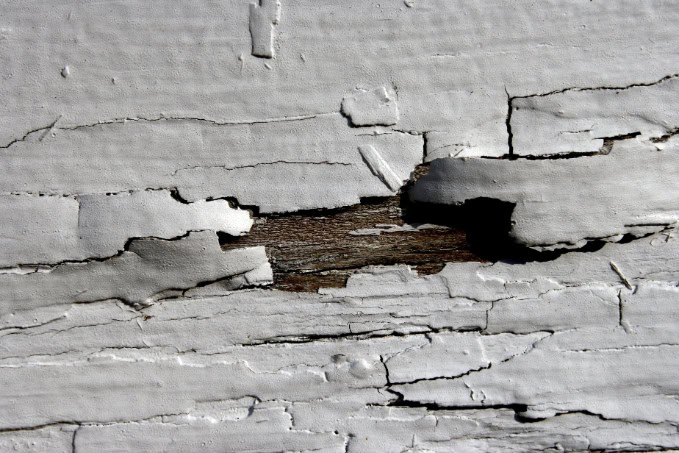 Peeling and cracked white paint on a wooden surface, revealing exposed wood underneath.