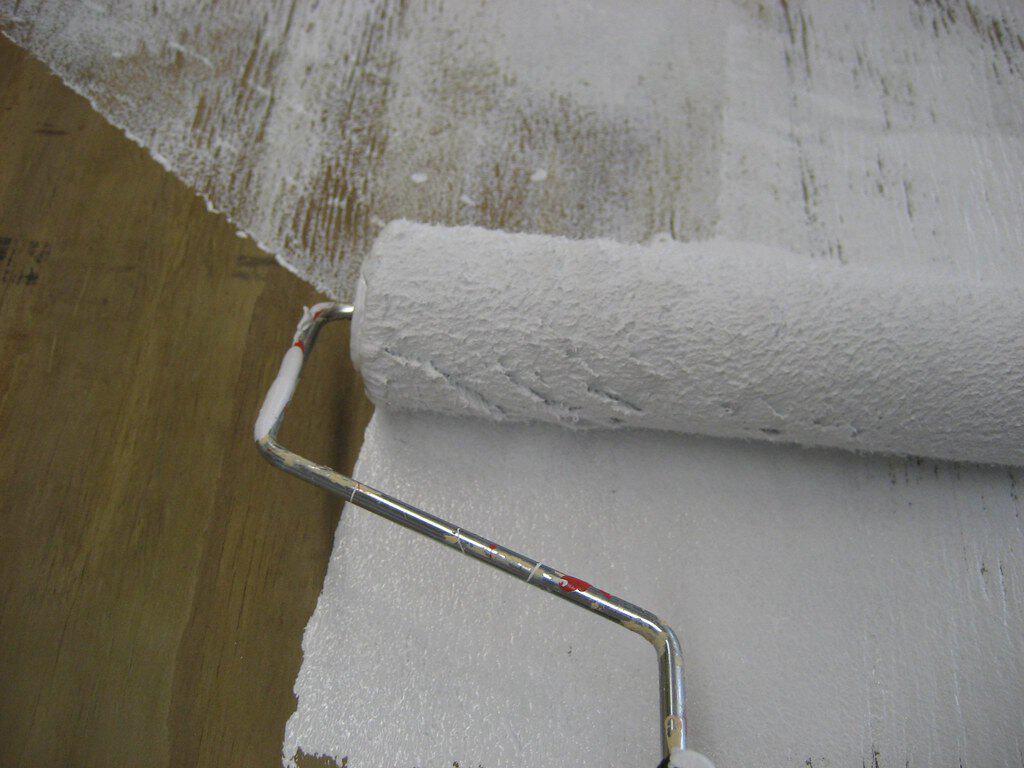 A paint roller applying a fresh coat of primer on a wooden surface, partially covering bare wood.