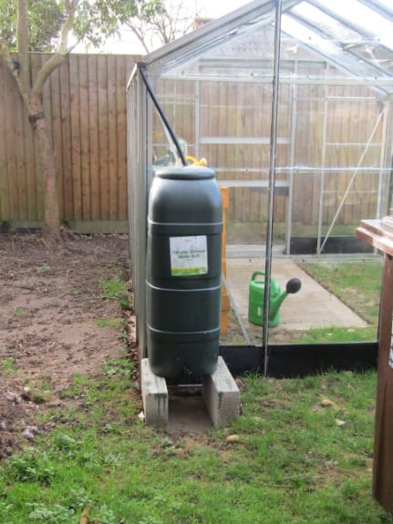 A water butt installed in a greenhouse gutter, collecting rainwater for garden use.