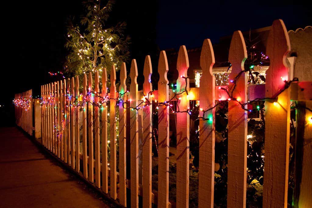 A festive display of Christmas lights draped over a wooden fence.