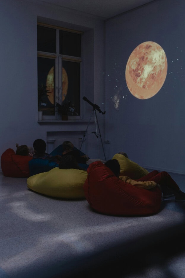 Children watching an astronomy projection on the wall with a telescope facing the window