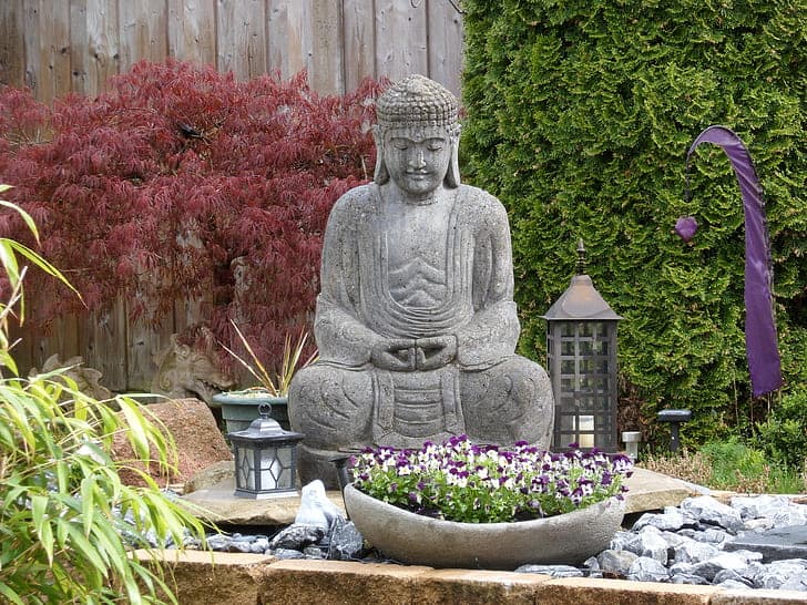 Gautama Buddha garden statue surrounded by plants and rocks.