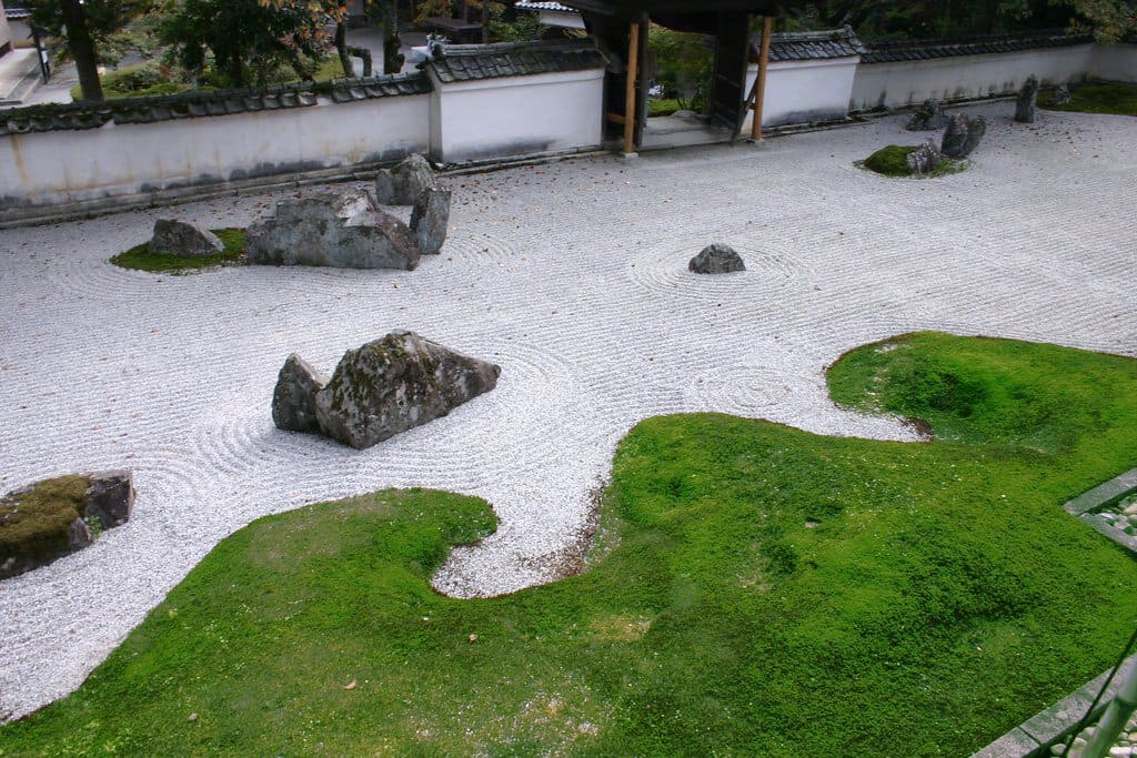 A moss resembling a coastline next to raked sand and rock sculptures.