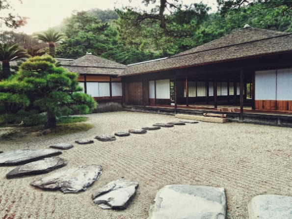 Stone paths spaced between raked sand in a Zen garden, leading to traditional Japanese houses.