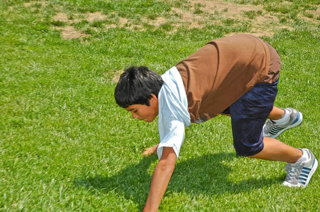 A child in a bear crawl position on a lawn.