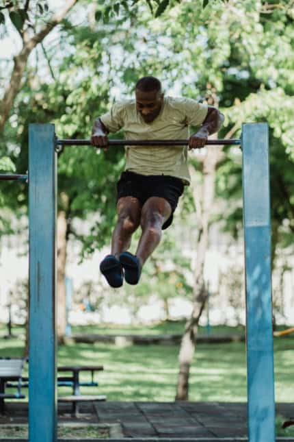 A man doing pull-ups on an outdoor monkey bar.