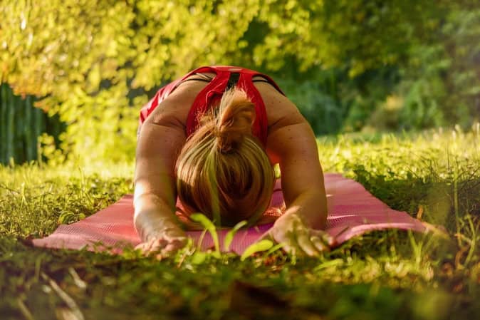 A woman stretching on her yoga mat outdoors as part of her garden gym workout routine.