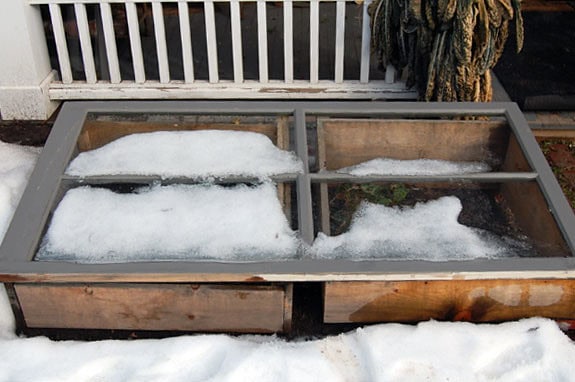 A wooden cold frame partially covered and surrounded by snow.