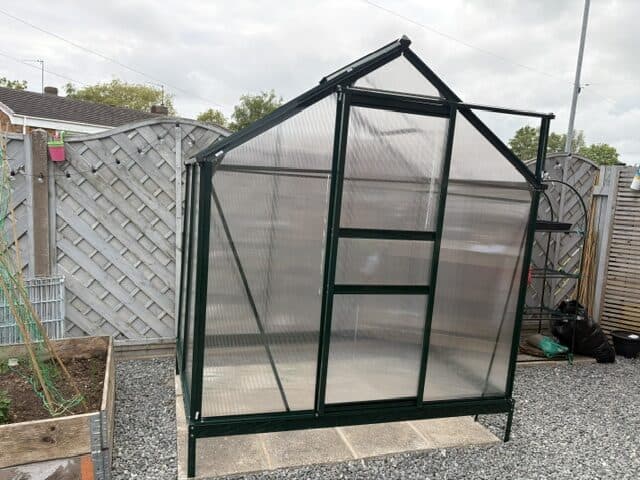 A metal garden greenhouse incorrectly standing atop its four anchoring pegs