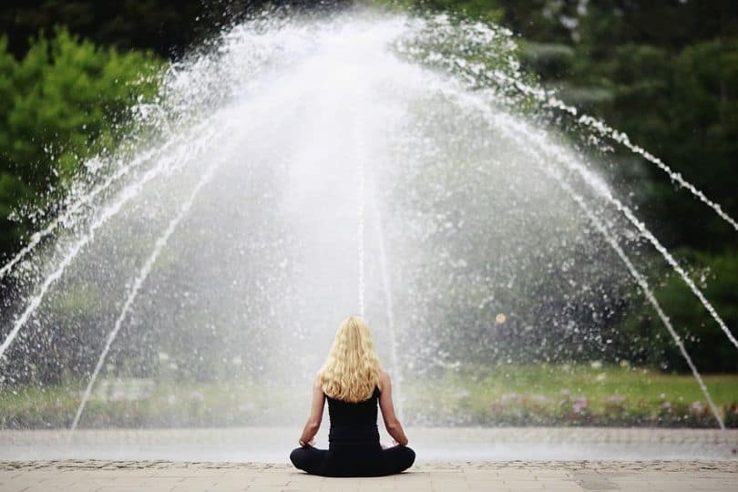 woman sat in a yoga pose in front of a fountain