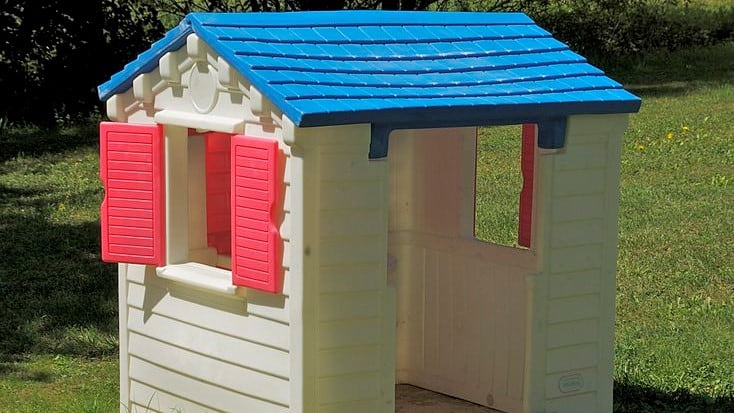 plastic playhouse in white and blue with red shutter windows on grass