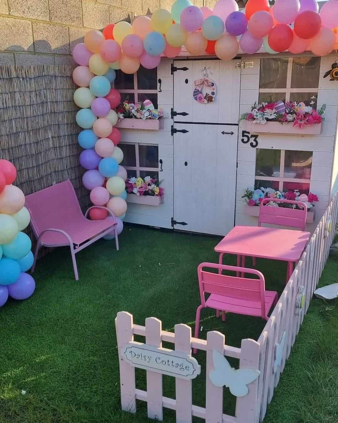 two storey barn door playhouse with picket fence painted white on astro turf with balloon arch around the door