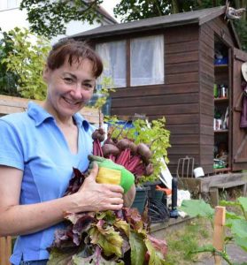 Sandra Lawrence of The Event Gardener in front of a shed smiling and holding vegetables