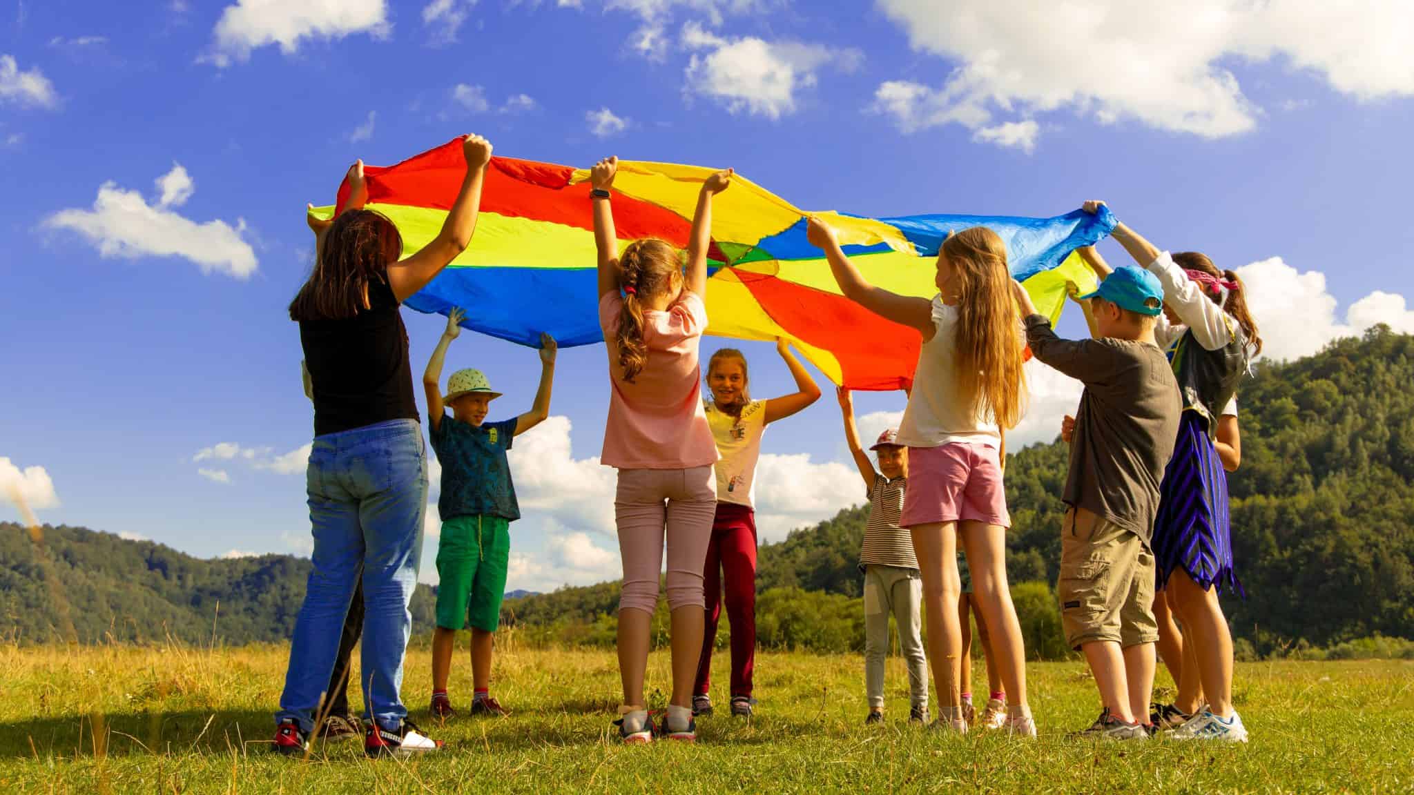 children playing under a multi-coloured parachute in a field