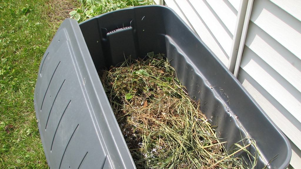 plastic compost bin with grass cuttings next to white clapperboard wall