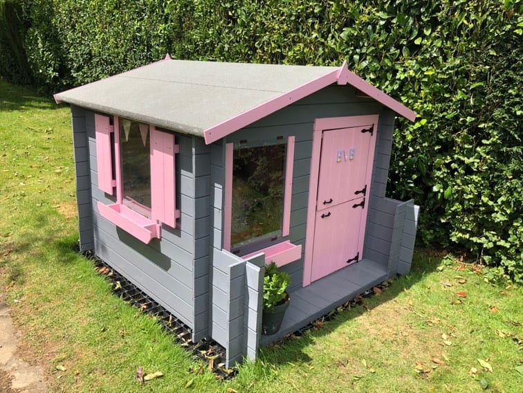 single storey pent roof playhouse with small porch painted pink and grey on grass