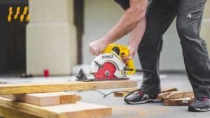 Man bent over holding a circular Dewalt saw cutting timber