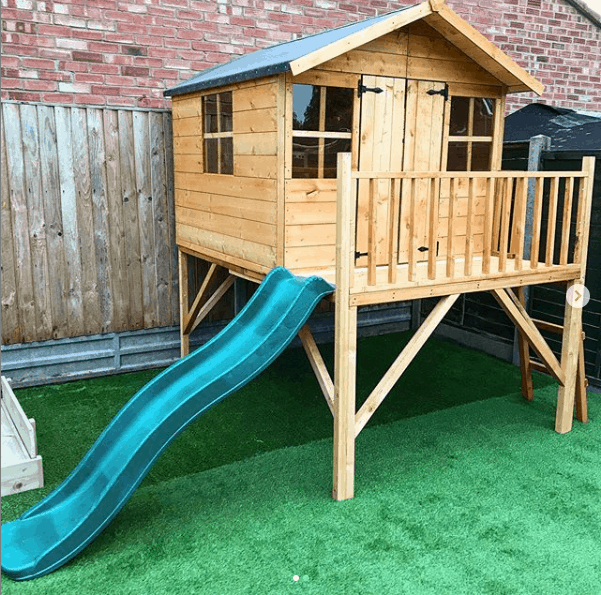 wooden tower playhouse with apex roof and slide and veranda on astro turf