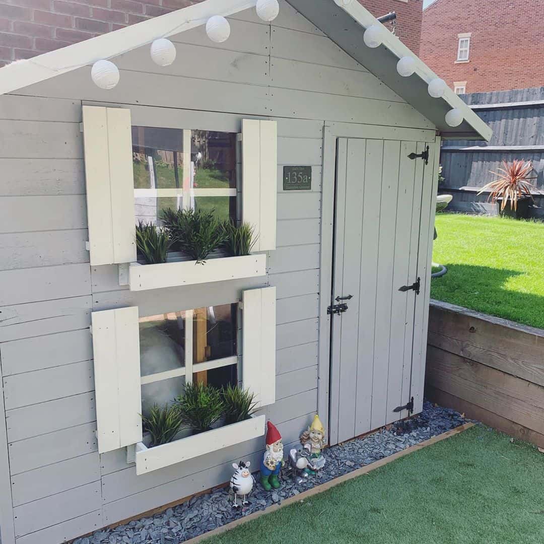 two storey pent roof playhouse with shuttered windows and window planters on astro turf on sunken level of garden