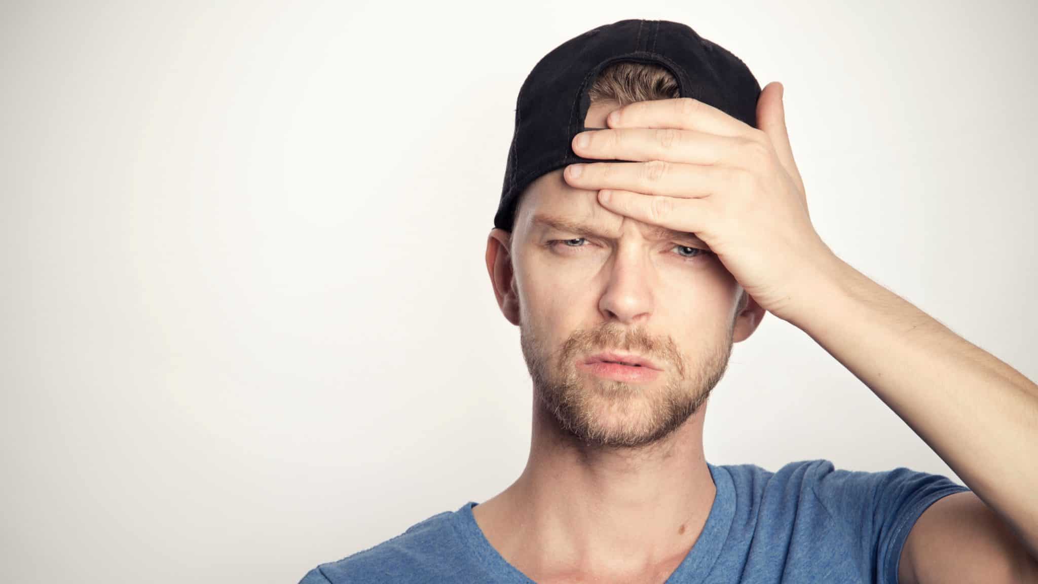 man wearing a backwards baseball cap looking confused with his hand to his head