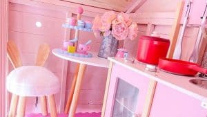 pink children's wooden playhouse interior with pink stool, table, and flowers